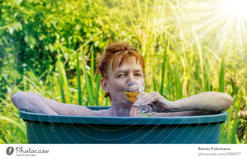 In high temperatures and sunshine in summer, a woman bathes in a rain barrel. In her hand she holds a glass of white wine. Human being Feminine Woman Adults