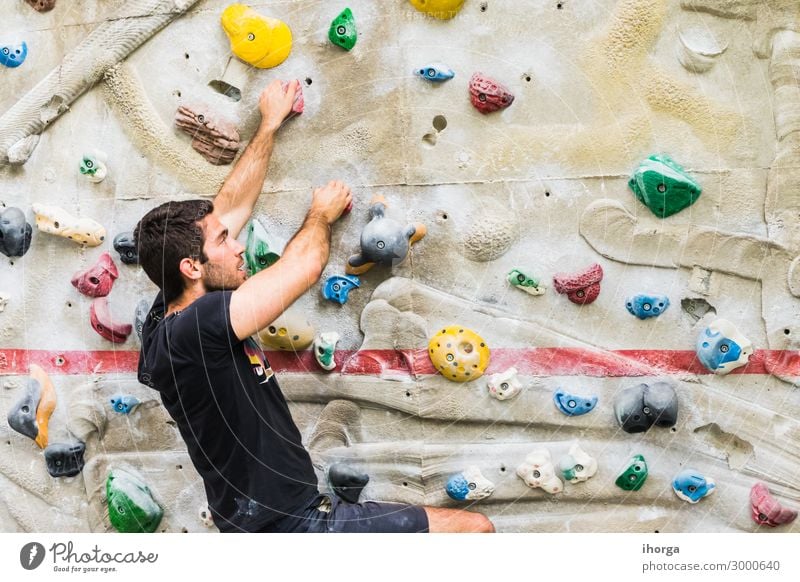 Beautiful young woman in black outfit climbing on practical wall in gym,  bouldering, extreme sport, rock-climbing concept Stock Photo