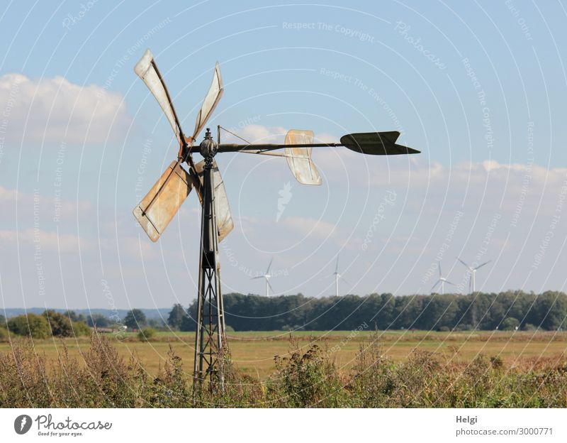 small historical windmill made of metal stands on a meadow, in the distance modern wind turbines Technology Energy industry Renewable energy Wind energy plant