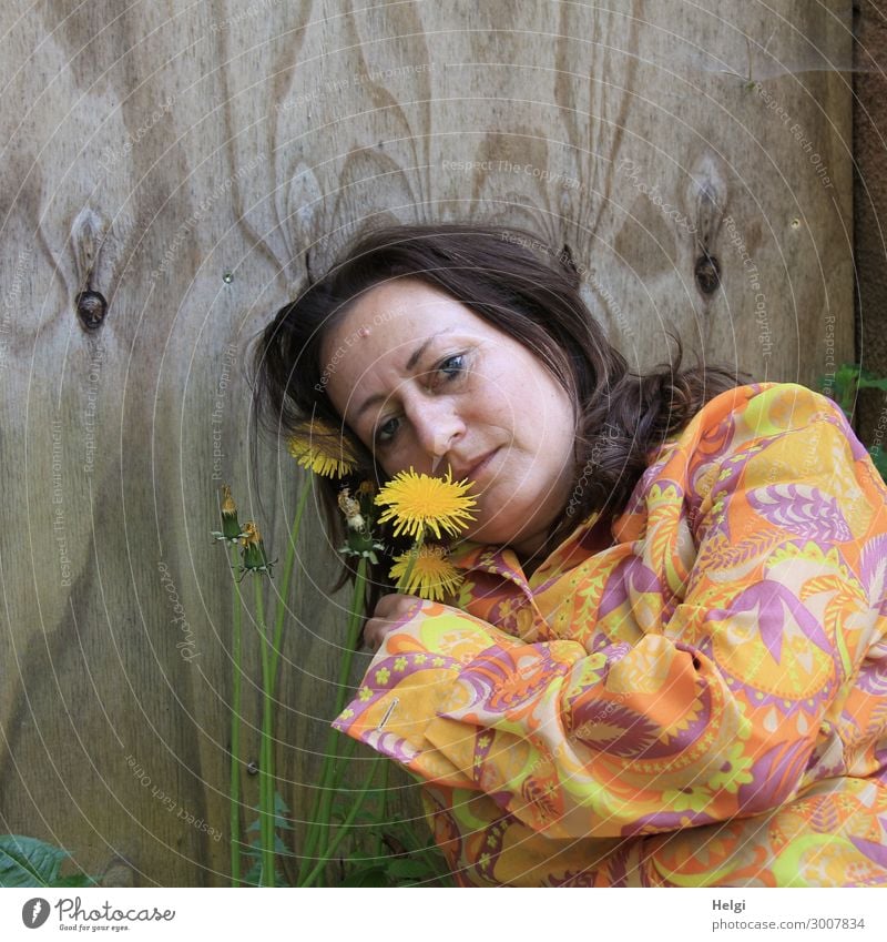 Portrait of a woman with long, brunette hair and colourful blouse holding a dandelion flower in her hand, in the background a wooden wall Human being Feminine