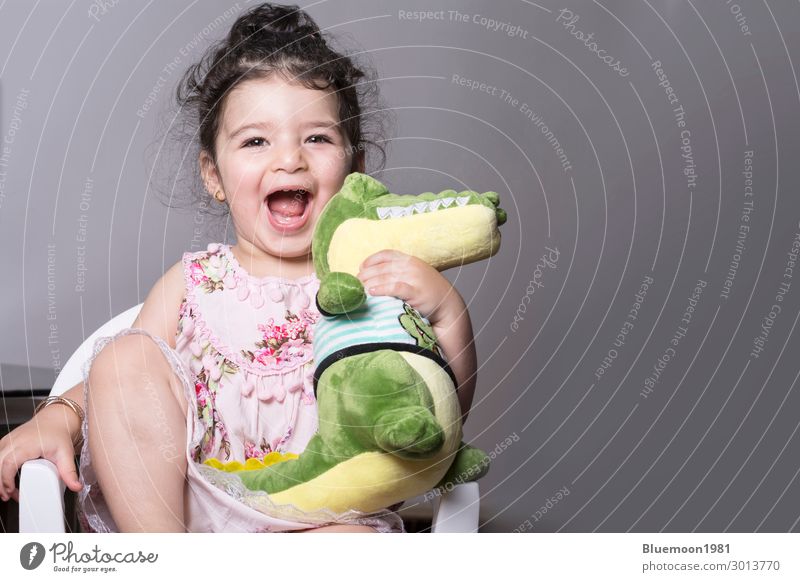 Surprised and happy little girl holding an alligator doll Lifestyle Joy Happy Beautiful Playing Chair Entertainment Child Girl Hand 1 Human being 1 - 3 years