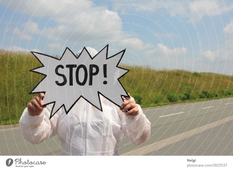 Person in a protective suit is standing on a street and holds a sign "Stop" in his hands Human being Adults Arm Hand Fingers 1 Environment Nature Landscape
