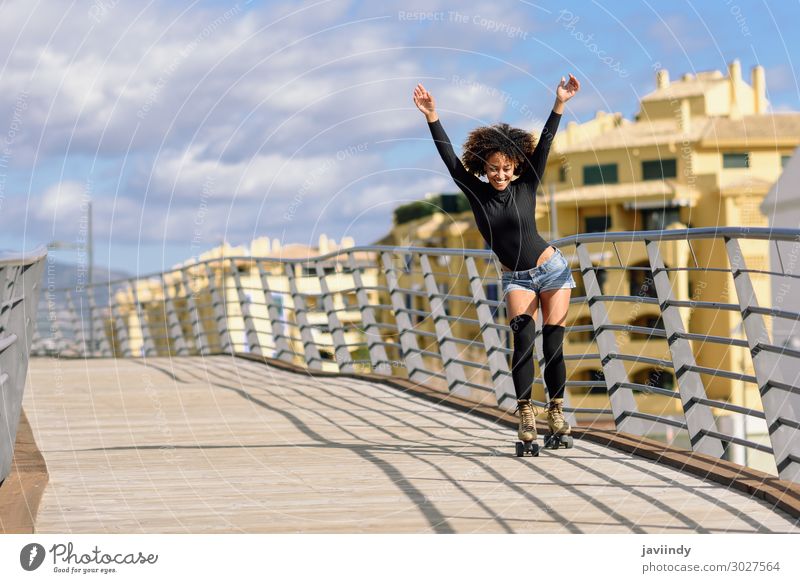 Black woman, afro hairstyle, on roller skates riding outdoors on urban bridge with open arms. Lifestyle Joy Happy Beautiful Hair and hairstyles