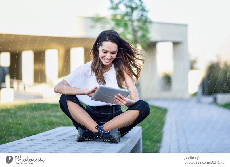 Young woman using digital tablet sitting outdoors in urban background. Lifestyle Happy Beautiful Reading Academic studies Work and employment Profession