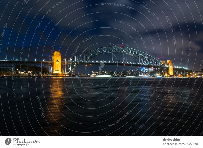 Sydney Bridge at night . In the foreground the sea. In the back of the picture the illuminated bridge with yellow illuminated pillars. Trip Summer Ocean Water
