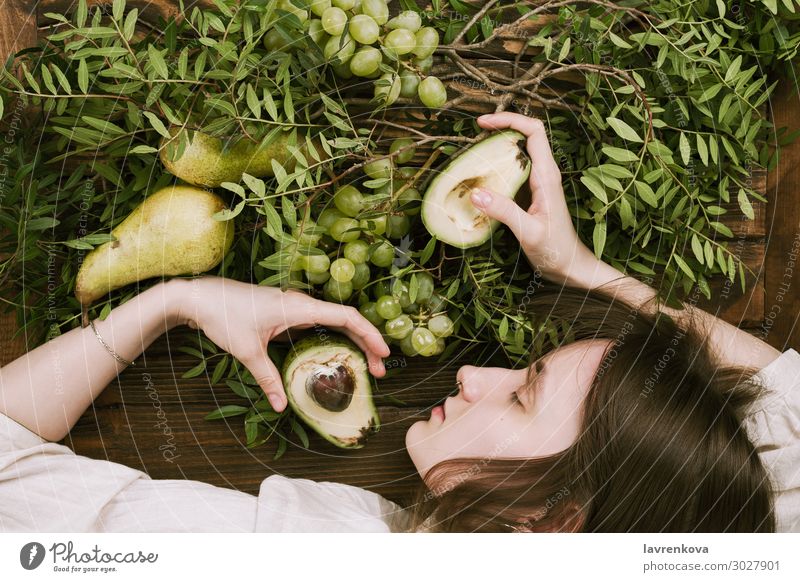 woman lying on wooden table holding grapes, pears and avocados Agriculture Avocado Branch Farm Woman flat lay Food Healthy Eating Food photograph Fresh Fruit