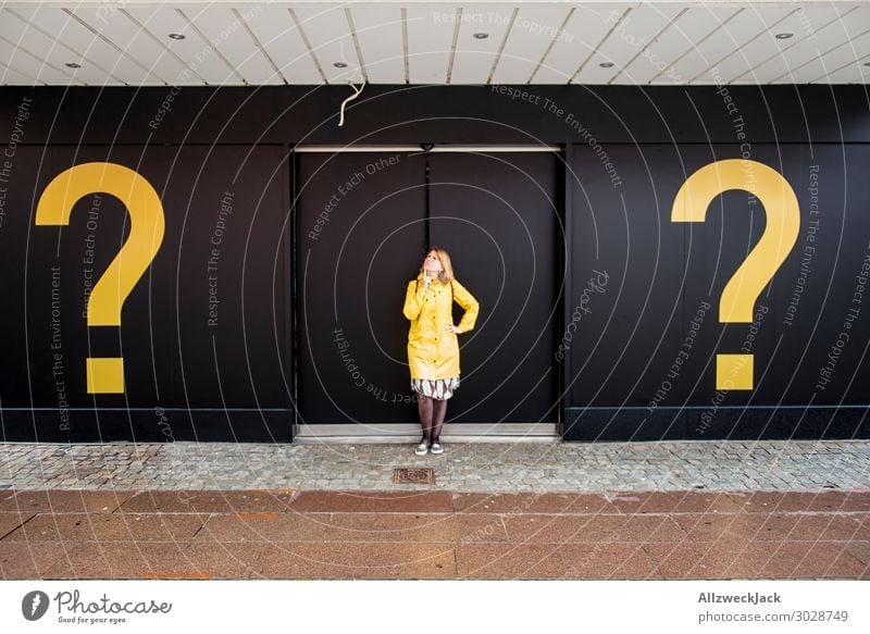 young woman with yellow rain jacket between two questionzichen Question mark Ask Decide Unclear Marvel Think Meditative 1 Person Central perspective Door Yellow