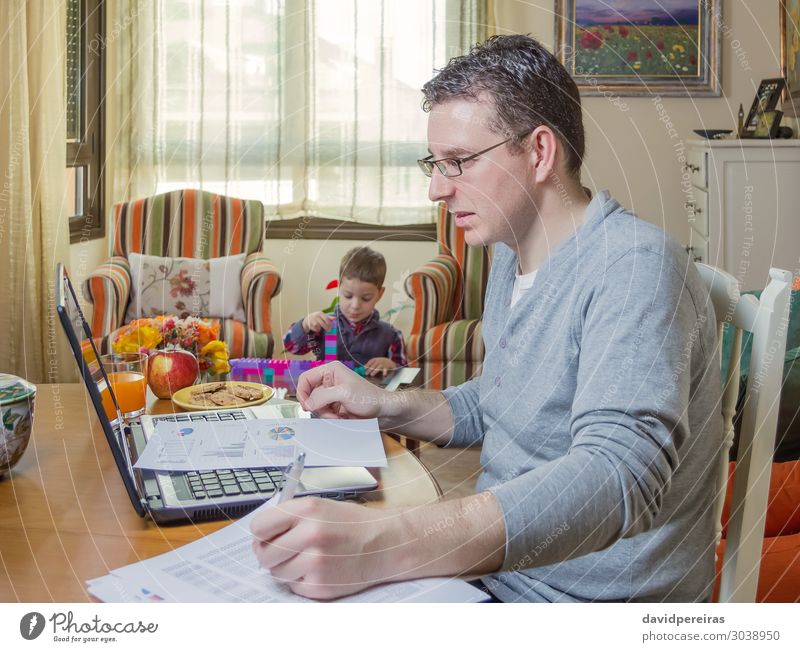 Father working in home office with notebook and his son playing on background Lifestyle House (Residential Structure) Sofa Child Work and employment Office