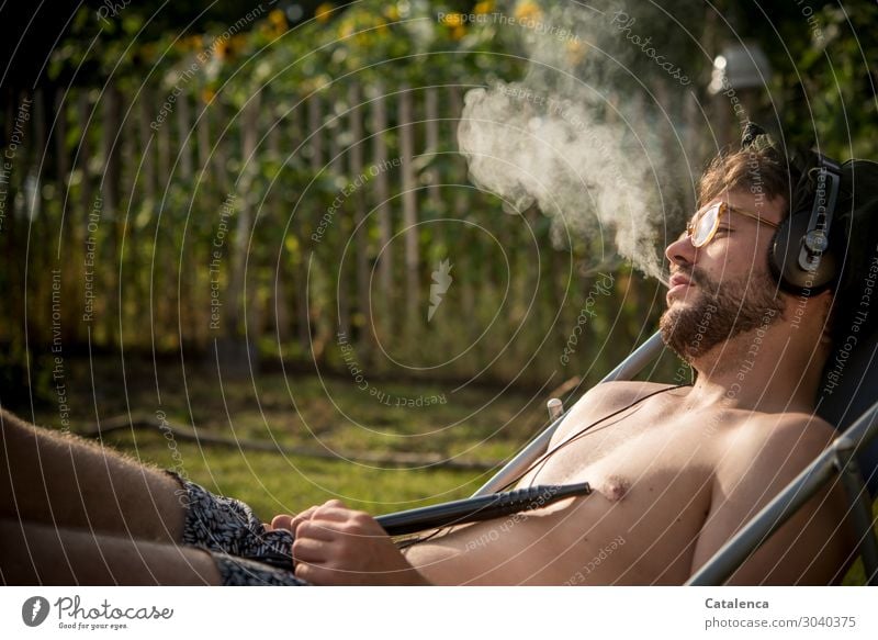 Relaxing, young man with headphones smoking in deck chair Smoking Intoxicant Listen to music Nature Plant Summer Beautiful weather Flower Grass Leaf Blossom