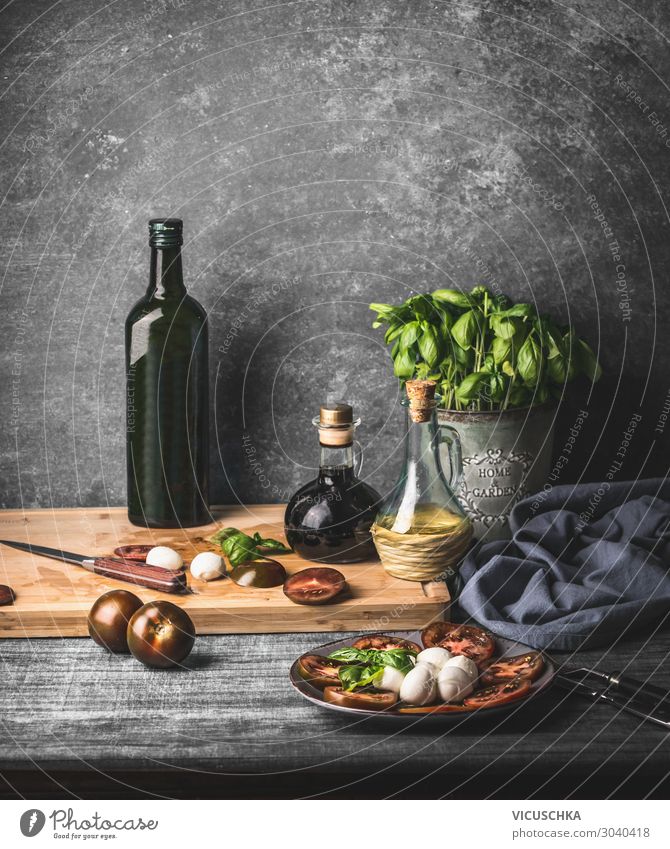 Still life with Italian caprese salad served on rustic table with potted basil kitchen herbs and bottle of olive oil on rustic table with ingredients still life