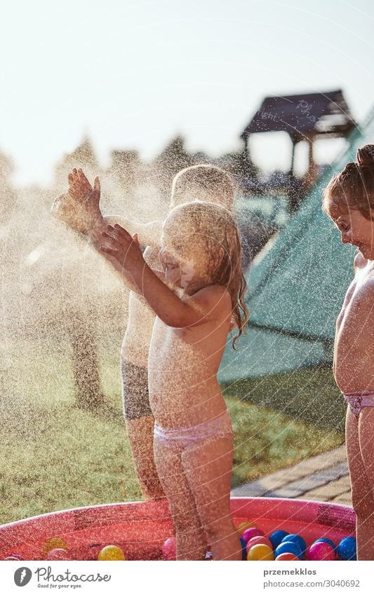 Little cute adorable kids enjoying a cool water sprayed by their father during hot summer day in backyard. Candid people, real moments, authentic situations