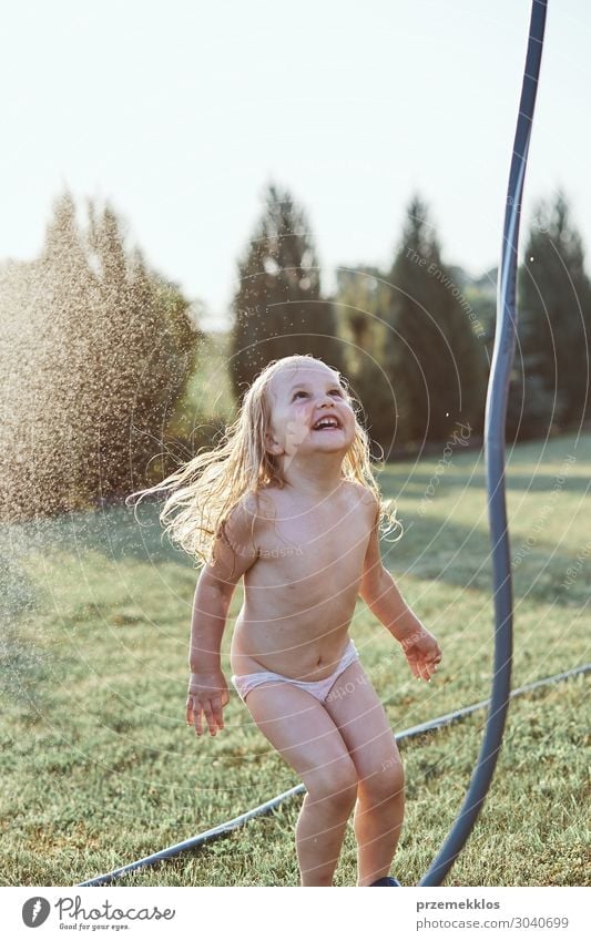 Little cute adorable girl enjoying a cool water sprayed by her mother  during hot summer day in backyard. Candid people, real moments, authentic  situations - a Royalty Free Stock Photo from Photocase