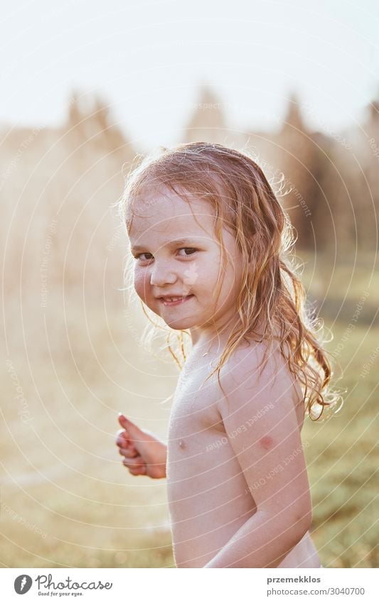 Little cute adorable girl enjoying a cool water sprayed by her mother during hot summer day in backyard. Candid people, real moments, authentic situations