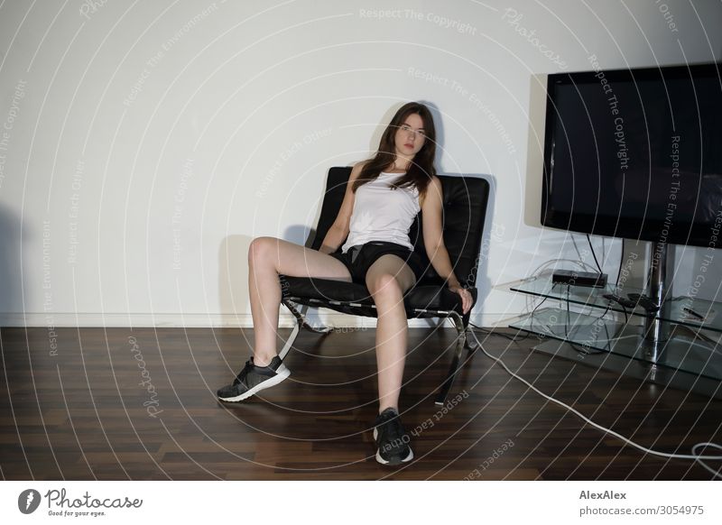 Young woman in an armchair next to a television set Lifestyle Style Living or residing Armchair Room TV set Classical modern Youth (Young adults) Legs