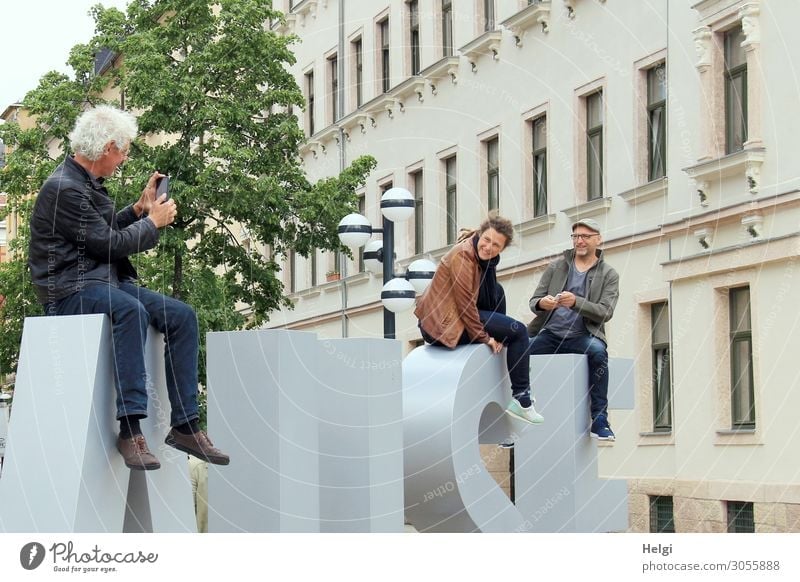 two men and a woman sit in front of a building on giant letters ,model and photograph each other with their smartphones PDA Human being Masculine Feminine Woman