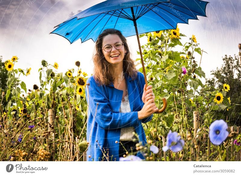 Smiling young woman with blue umbrella and sunflowers in background Feminine Young woman Youth (Young adults) 1 Human being Plant Drops of water Sky Clouds