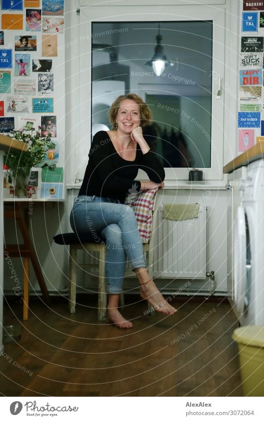 Young woman sitting on the side of a chair in her kitchen and smiling - student cake Lifestyle Joy already Well-being Decoration Chair Table Window