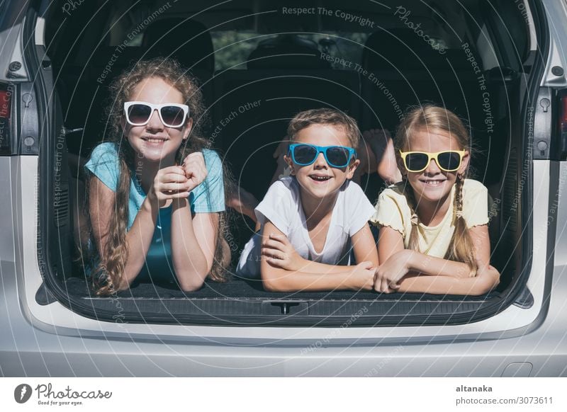 Happy brother and his two sisters are sitting in the car at the day time. Children having fun outdoors. Concept of the family is ready for travel. Lifestyle Joy