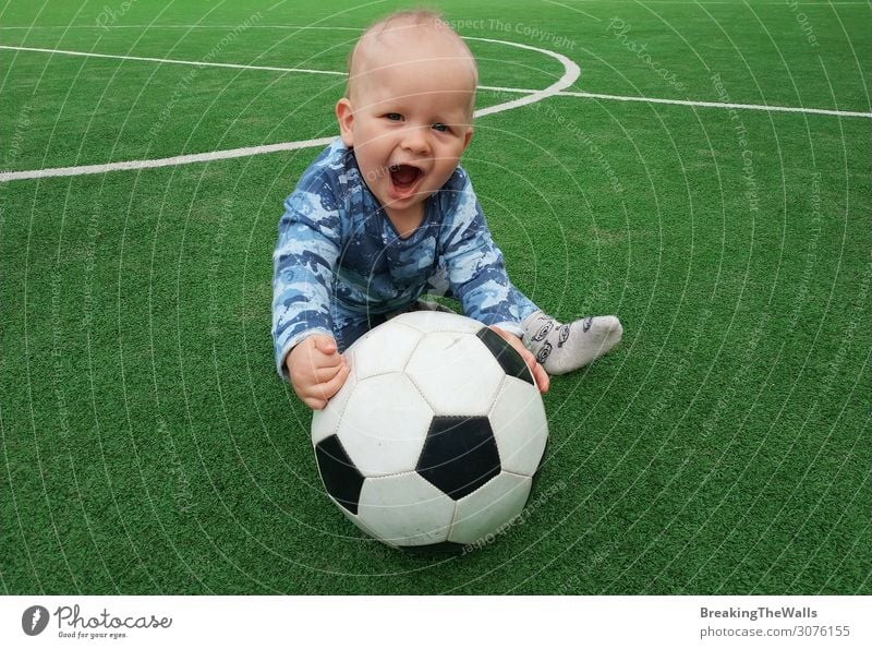 Little boy sitting on green grass of playing field with soccer football ball and looking at camera Lifestyle Leisure and hobbies Sports Soccer Foot ball Ball