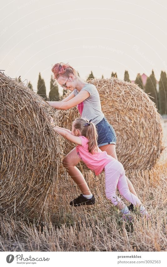 Sisters, teenage girl and her younger sister pushing hay bale playing together outdoors in the countryside Lifestyle Joy Happy Relaxation Leisure and hobbies