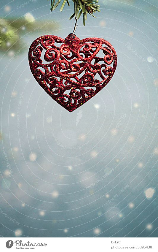 Red, filigree Christmas decoration as a heart with an oriental pattern, hangs on a fir branch in the snow. Christmas tree pendant in the shape of a heart, hangs on a Christmas tree branch with snowflakes. Beautiful, cheerful, curved Christmas decoration and ornament.