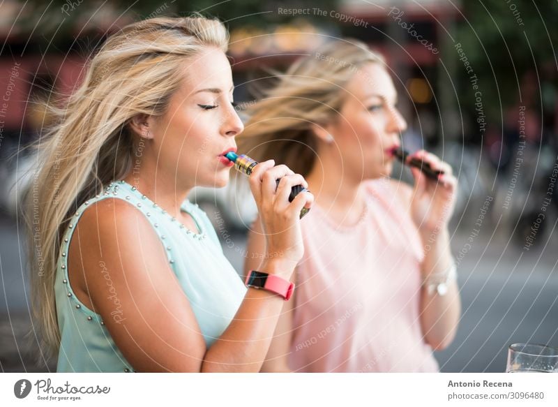 two blonde sister with e-cigar smoking in bar terrace Lifestyle Elegant Beautiful Leisure and hobbies Technology Human being Woman Adults Hand Street Fashion