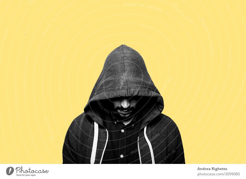Concept of hacker, cyber threats, young depression, adolescence difficulties. Young caucasian male student staring at the floor with the eyes hide hided by a hood. Yellow background