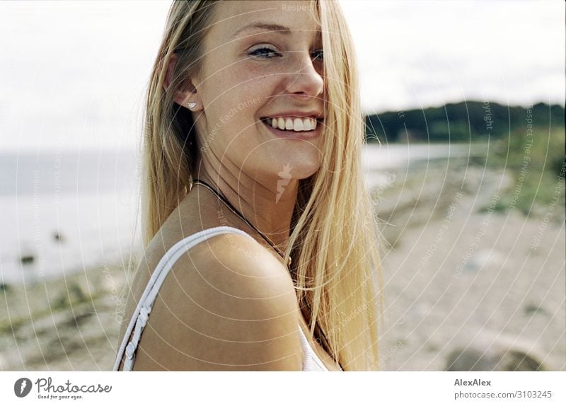Young, tall woman sits in a summer dress on the beach of the Baltic Sea and  smiles - a Royalty Free Stock Photo from Photocase