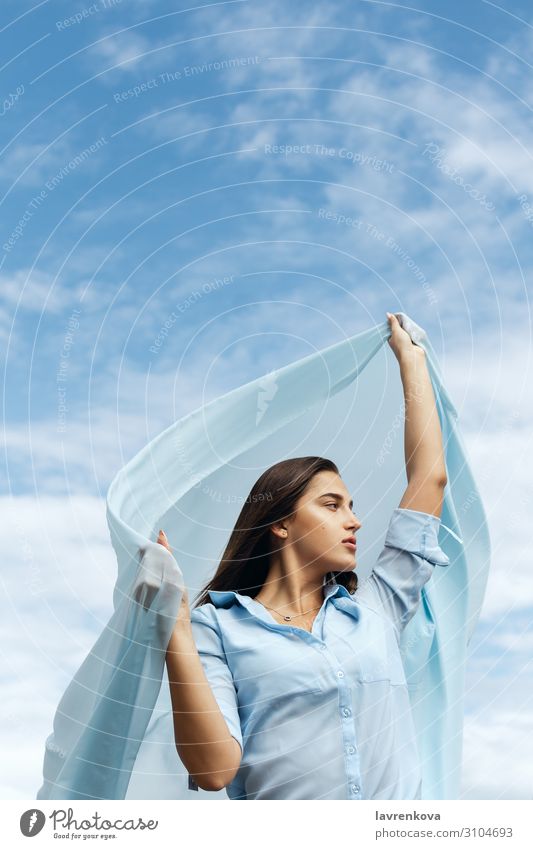Young female holding cut of blue cloth up in the sky Adults Air Loneliness Attractive Blue Cloth Clouds Cut Woman Freedom Young woman Hand Happy Height Horizon