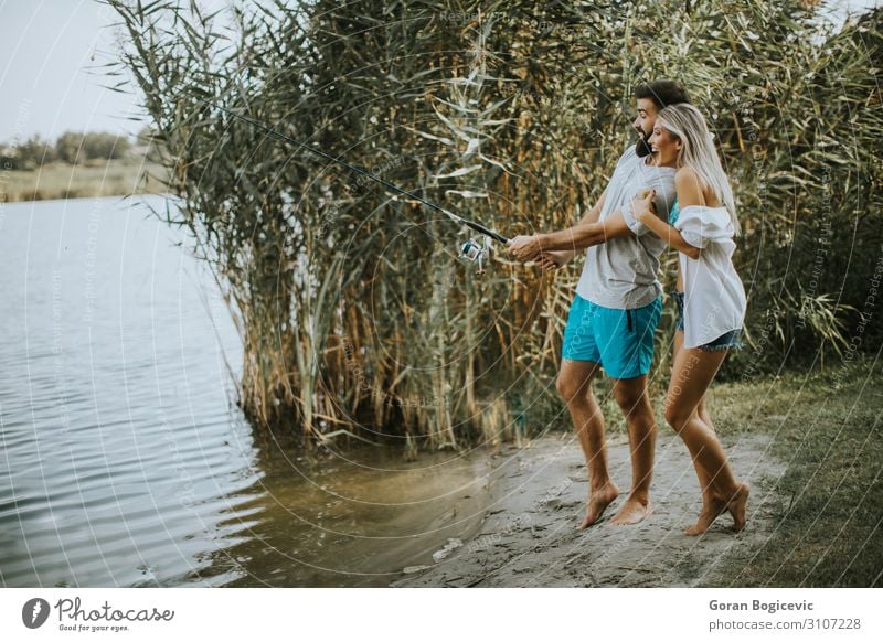 Young couple enjoying fishing on sunny day at a calm lake Lifestyle Happy Beautiful Relaxation Leisure and hobbies Camping Summer Sun Entertainment Woman Adults