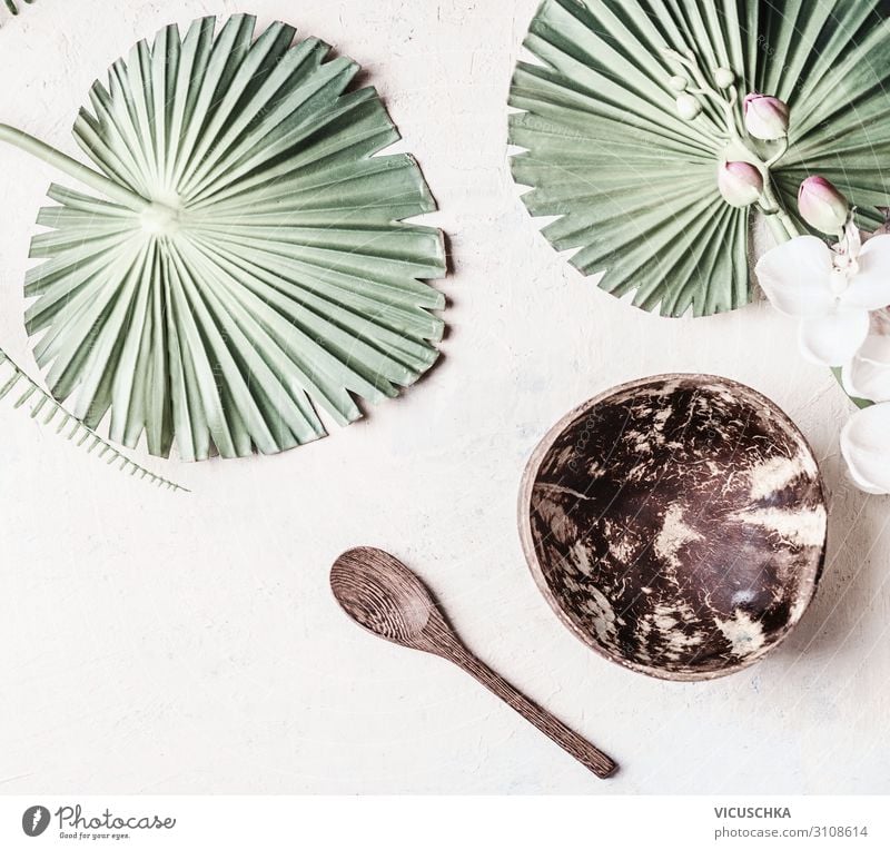 Empty coconut bowl with spoon on white desk background with tropical leaves, top view. Copy space for your design or product empty copy creative above style