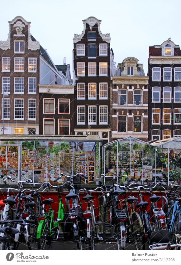A row of bicycles, behind them greenhouses, behind them the typical narrow buildings of downtown Amsterdam Sightseeing City trip Netherlands Downtown Old town
