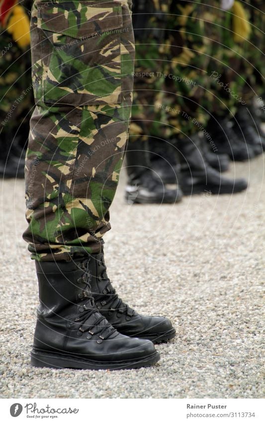 Legs of a soldier in uniform with camouflage colours during a ceremony. More soldiers in the background. Soldier military Masculine Man Adults Feet