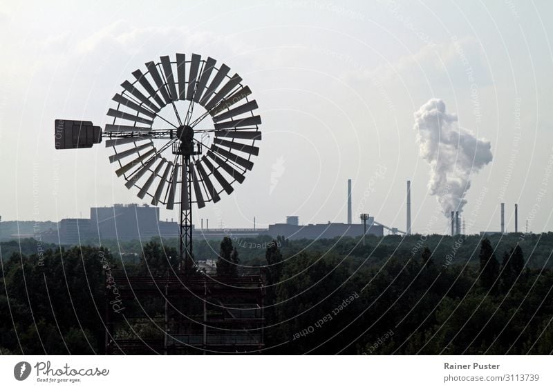 A wind turbine turns in the wind against a background of chimneys and industry. Factory Industry Energy industry Renewable energy Wind energy plant