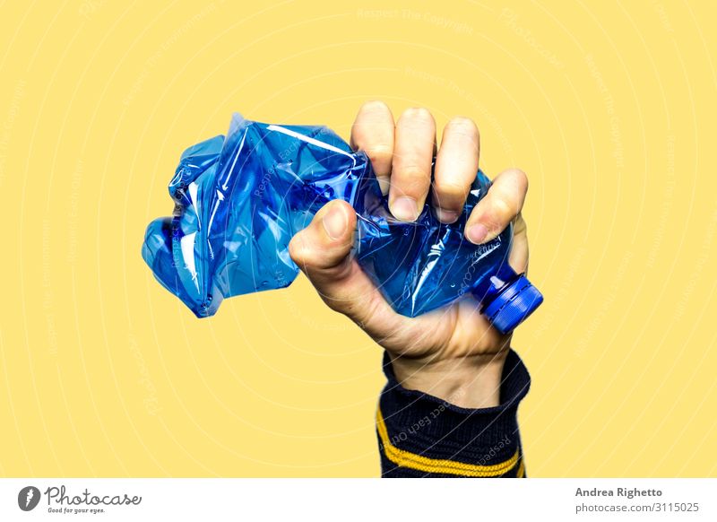 Concept of stop plastic pollution, global warming, recycling plastic, plastic free. Hand tightly squeezes an empty blue plastic bottle in a sign of protest. Yellow background with an isolated subject