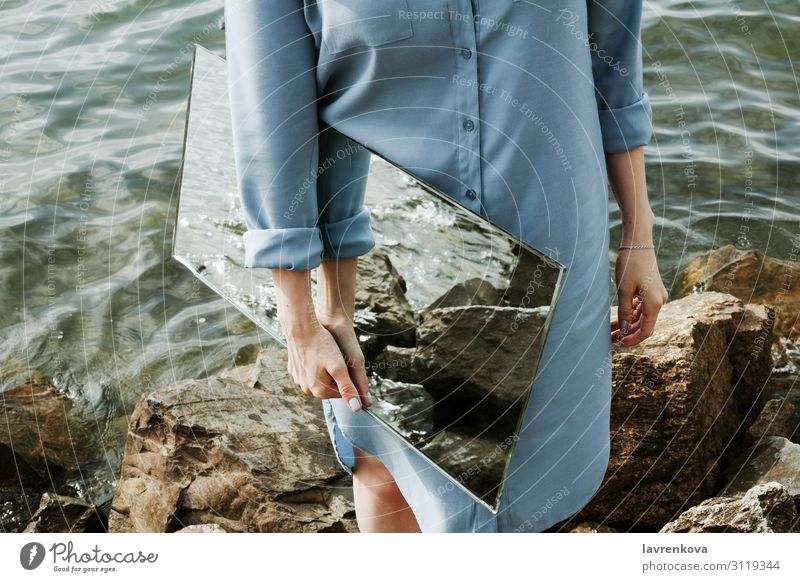 woman standind on a shore in blue dress holding a mirror Environment Clean Nature Conceptual design Adults Rock Waves Horizontal Faceless Dress Coast Reflection