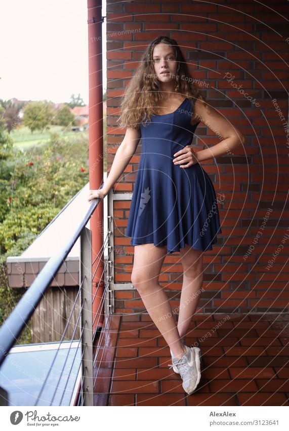 Portrait of a young, tall woman on a balcony with a brick wall and