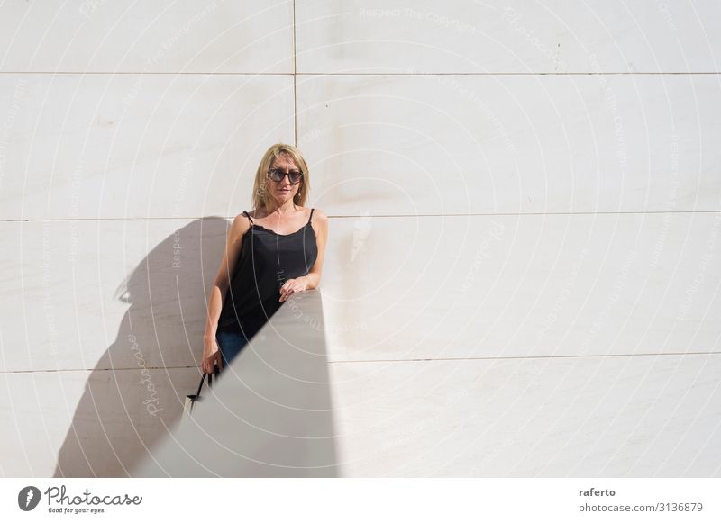 Blonde woman leaning on a white wall while looking camera Lifestyle Style Happy Beautiful Body Face Leisure and hobbies Summer Human being Feminine Young woman