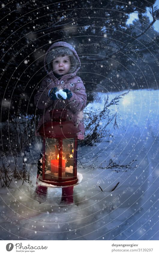Child hold christmas lamp with glass and candle inside in the night to pine tree. Winter Snow Decoration Lamp Christmas & Advent Snowfall Tree Candle Old Dark