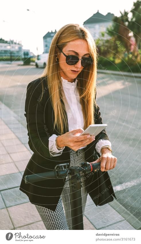 Businesswoman with e-scooter looking at cellphone Elegant Style Beautiful PDA Human being Woman Adults Transport Street Fashion Sunglasses Modern urban mobile