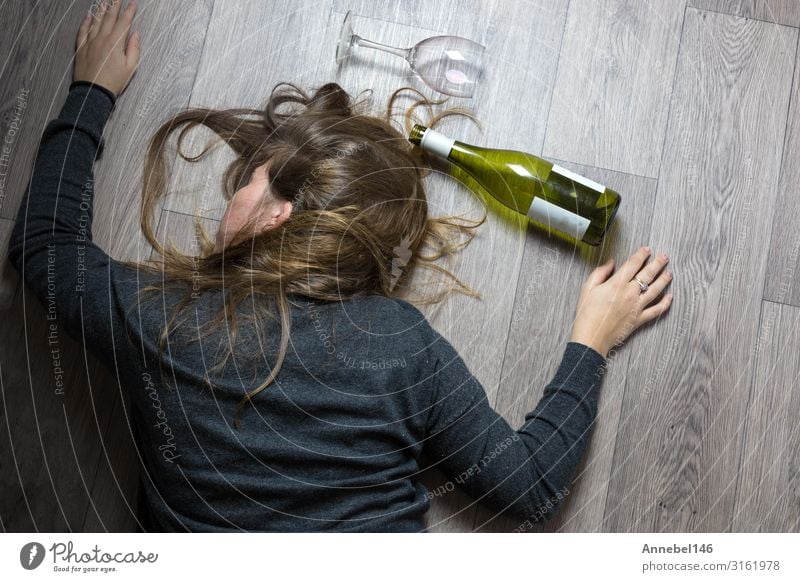 Drunk alcoholic young girl lying on the floor feeling sick by drinking red wine, empty glass and bottle knock-out Alcoholic drinks Lifestyle Illness