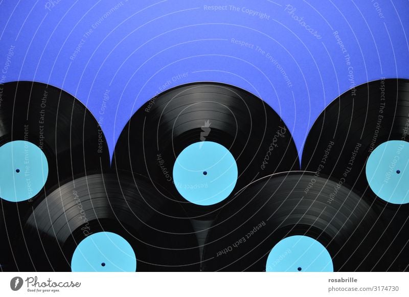 five old black vinyl records laid on top of each other with empty turquoise label on blue background as a band below with space for text above| symmetry Record