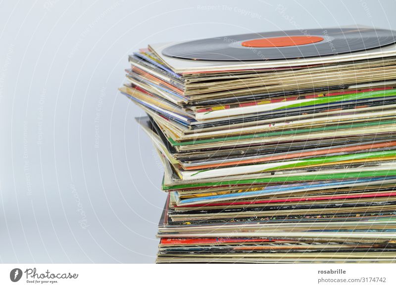 Stack of many old colorful vinyl record sleeves on top of each other with a black record on top with a neutral orange label in front of a white background with free space for text on the left | old