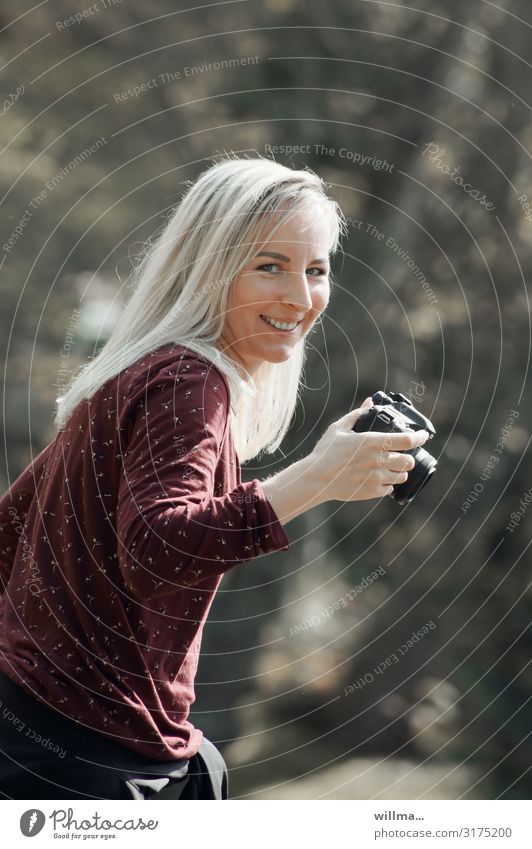 Young blonde amateur photographer smiles mischievously at camera Young woman Woman Photographer Blonde Long-haired Laughter Friendliness Camera Smiling Funny
