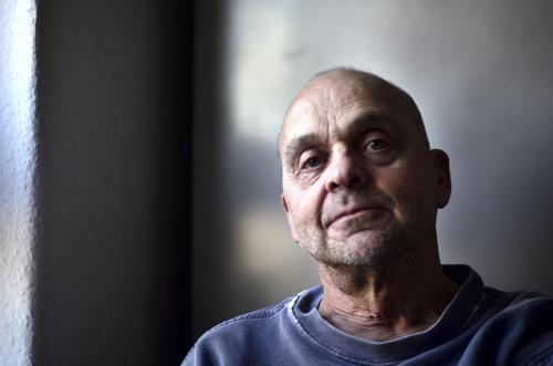 All-natural frontal portrait of a mature man with near-baldness, illuminated by soft, sidelong daylight, looking slightly from above, serious, profound and fearless directly into camera