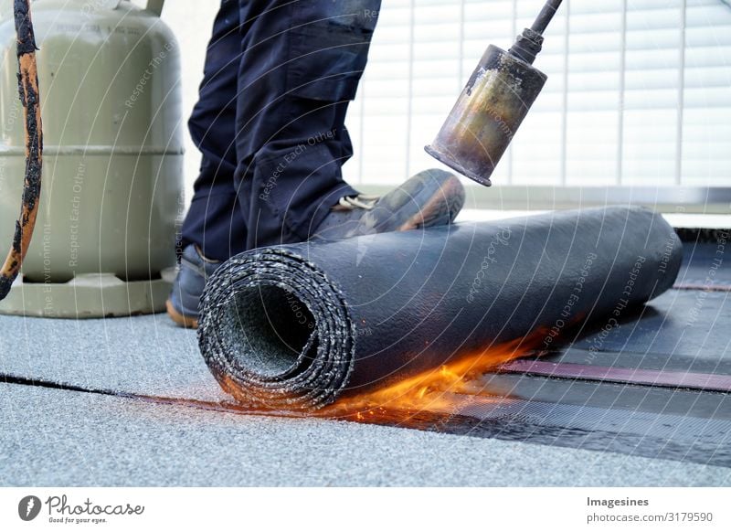 Flat roof installation with roofing felt, propane gas burner gas bottle. Construction work with roofing felt. Heating and melting of bitumen tar paper. Roof sealing