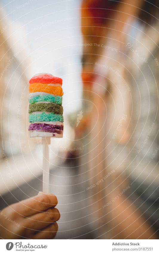 Hand holding delicious rainbow cake on city street Food Desert Cake Rainbow Multicoloured Bright sweetness Meal Nutrition To feed Tasty Delicious appetizing