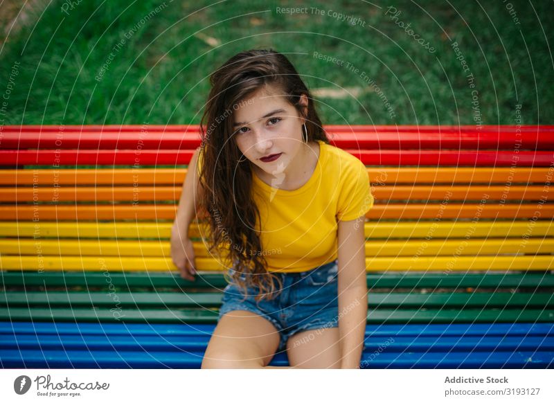 Cheerful woman sitting on rainbow bench Woman Bench Park Smiling Looking into the camera Sit Rainbow Easygoing Lifestyle Leisure and hobbies