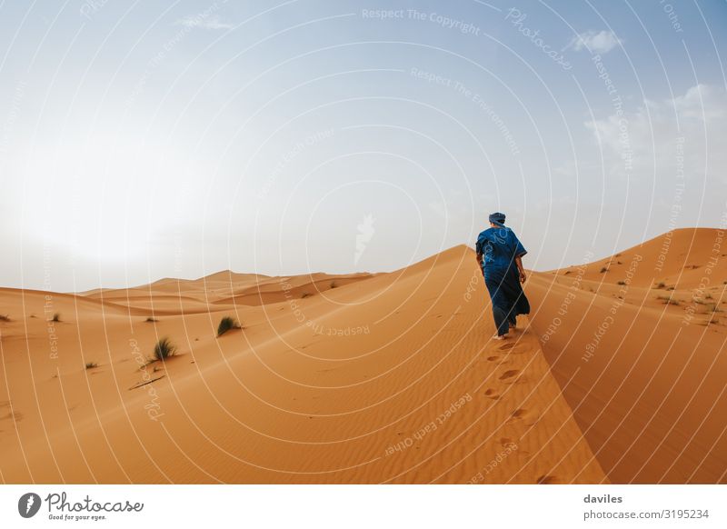 Arabian man in blue clothes walking on a desert dune. Lifestyle Exotic Vacation & Travel Tourism Trip Adventure Expedition Sun Human being Man Adults 1