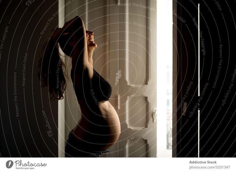 Pregnant lady near open door Woman To enjoy Door Open Home Bra Showing one's bellybutton Light expecting tummy Stomach Abdomen maternity awaiting Anticipation